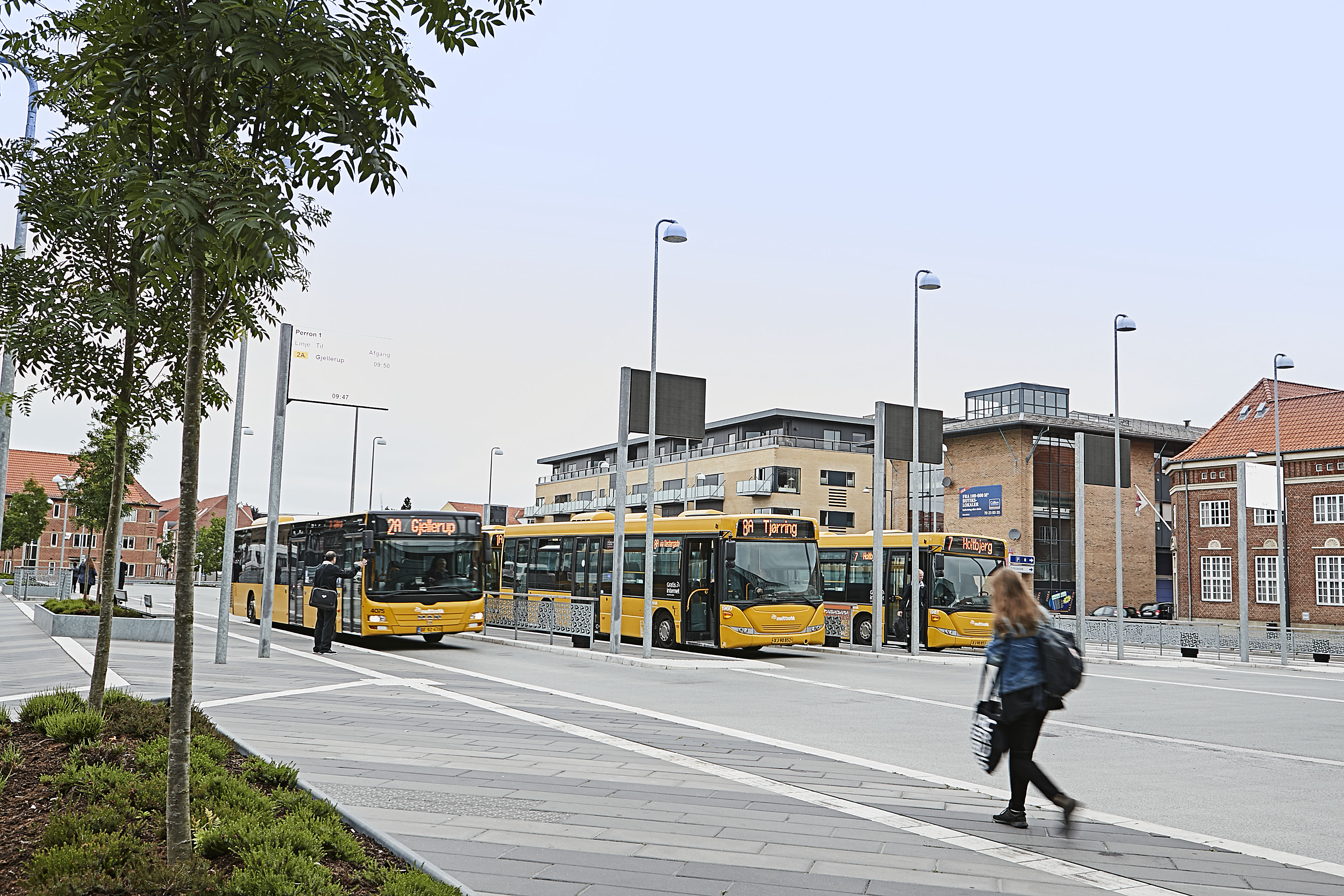Billede af busterminal I Herning med tre gule bybusser, kunder og chauffører.