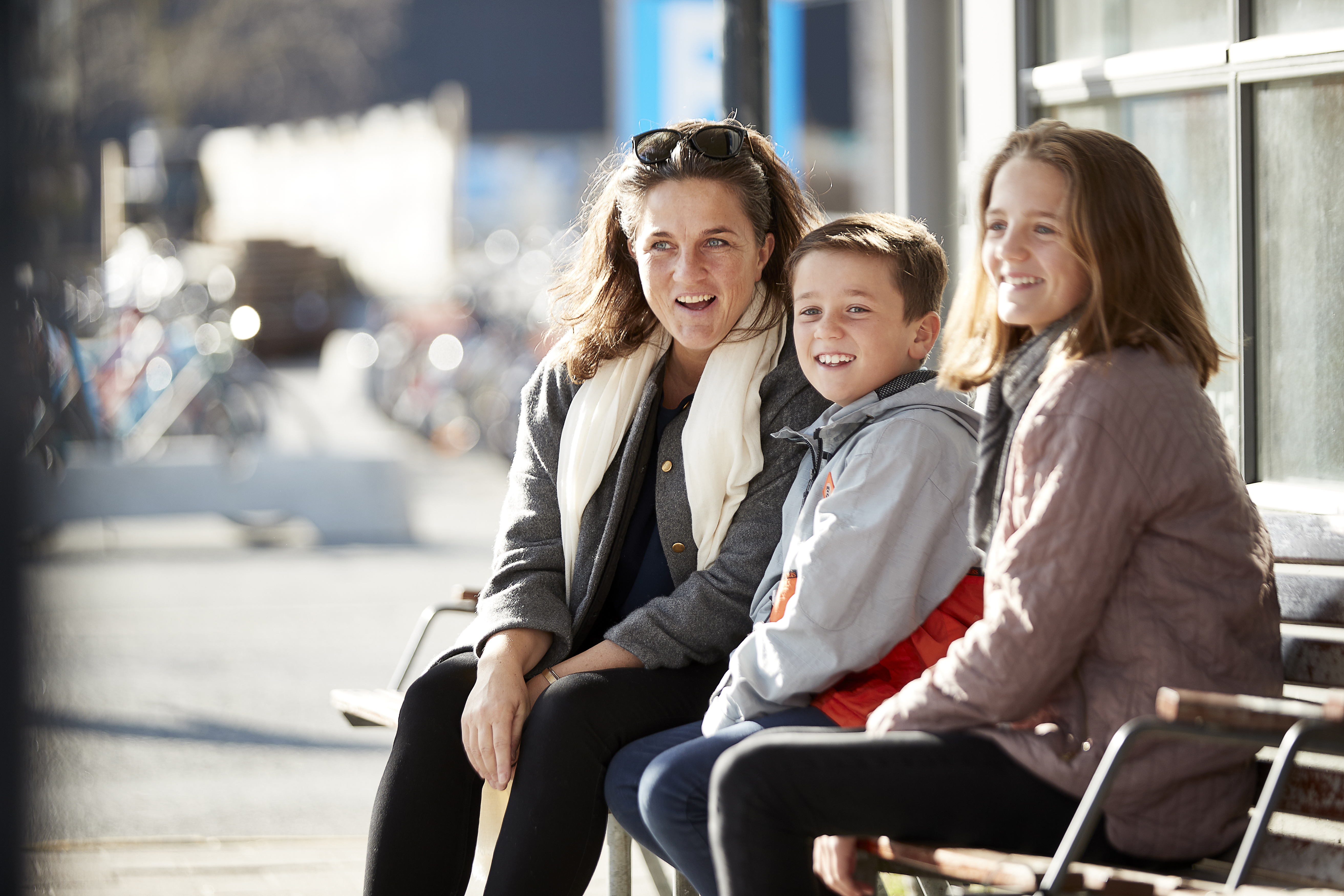 Billede af mor med to børn på en bænk ved en busterminal.
